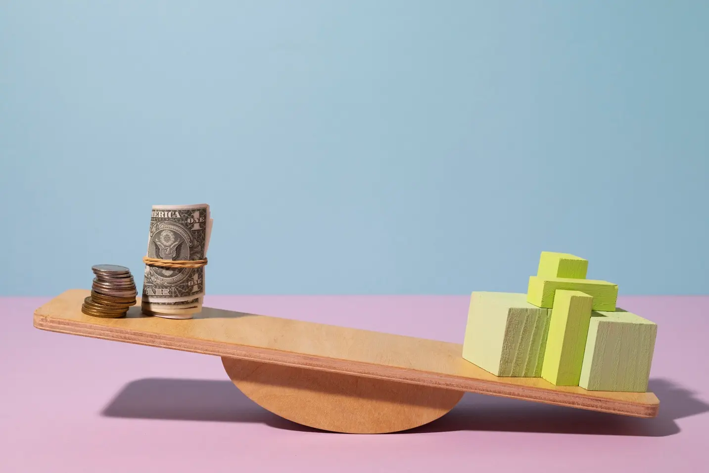 Une bascule en bois avec d'un côté des pièces et des billets, de l'autre des blocs colorés qui font pencher la balance, illustrant la notion de valeur comparée au prix.